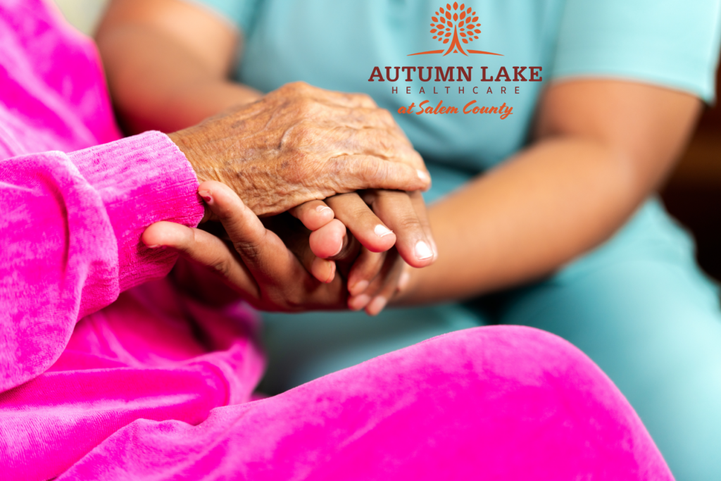 A caregiver holding the hand of an elderly resident in a supportive gesture at Autumn Lake Healthcare at Salem County.